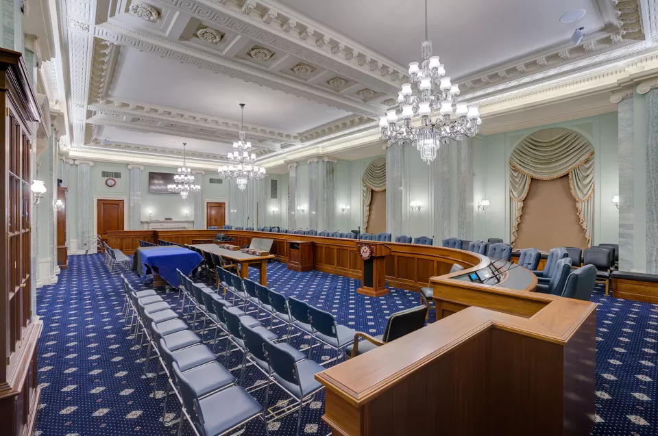 The finished hearing room features a three-legged custom wooden witness table (center), which was specially designed without legs on one side to provide an extended span to accommodate several witnesses. The custom carpeting was also inspired by the diamond pattern in the room’s historic marble flooring.