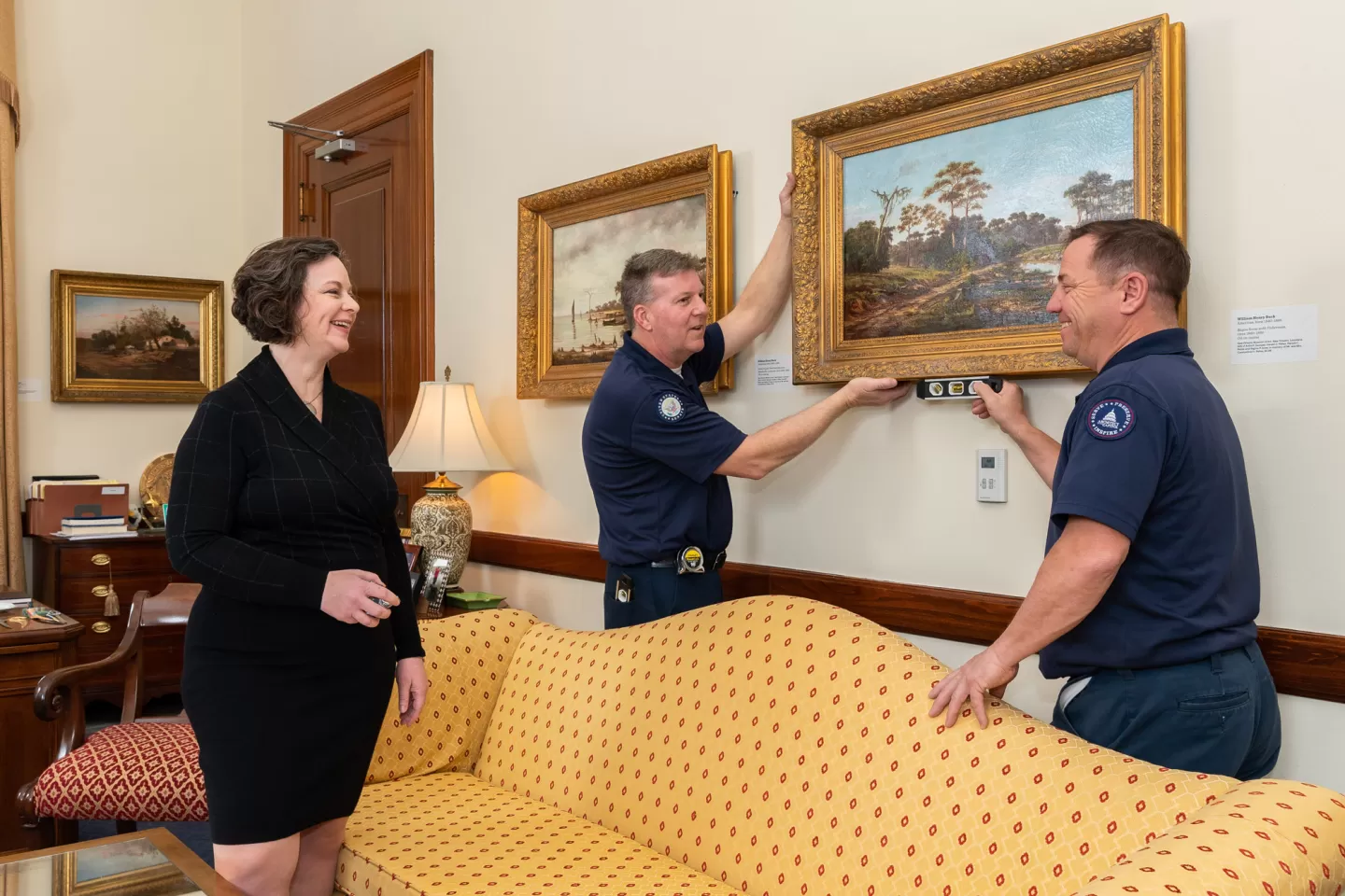 Senate Move Coordinator Bonnie Holod, who is also the supervisory architect in the Senate Office Buildings jurisdiction, works with Michael Gass and Paul Bosch, wood crafters with the Senate Wood Crafting Branch, to hang artwork in a senator's office.