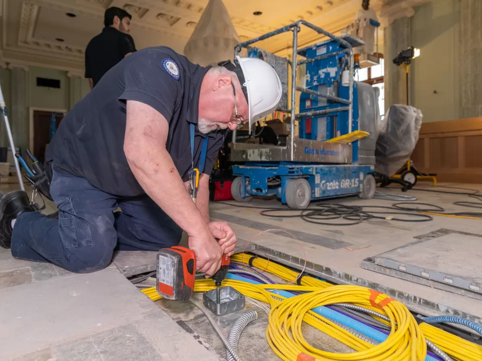 Scott Johnson, an electrician with the Senate Electrical Branch, installs new cabling in the in-floor raceway, the trough for essential electrical, IT and audiovisual infrastructure running below the hearing room floor.