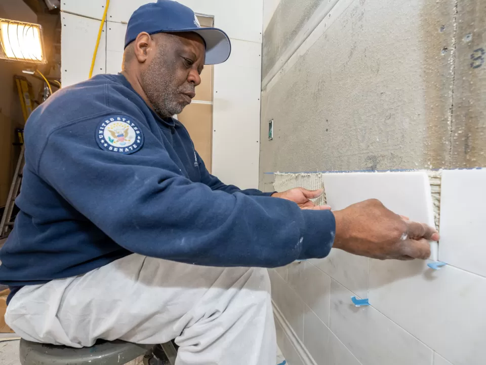Warren Campbell, a mason with the Senate Masonry Branch, sets marble tile in the renovated ADA-compliant restroom, with the tile selected to match the standard of the Russell Building restrooms.